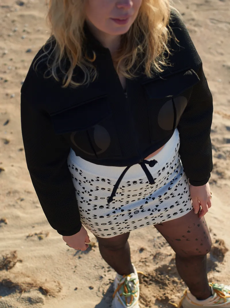 A Moontian in a black jacket and monogram shorts on the sand